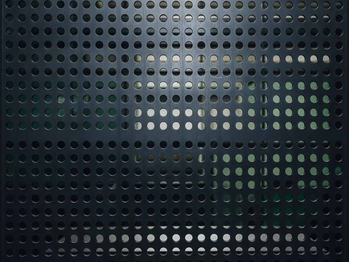 Regular array of round perforations in a dark metal panel — spacing alone, the first property of a seat mounting pattern